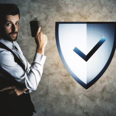Businessman holding smartphone on concrete wall background with digital abstract antivirus shield. Guard concept
